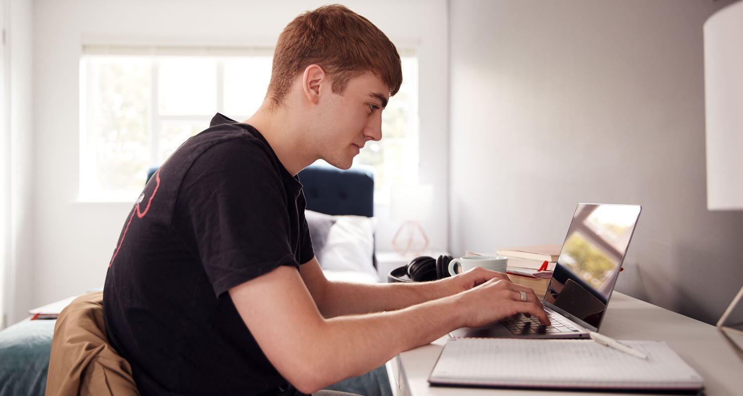 Male College Student In Shared House Bedroom Studying Sitting At Desk