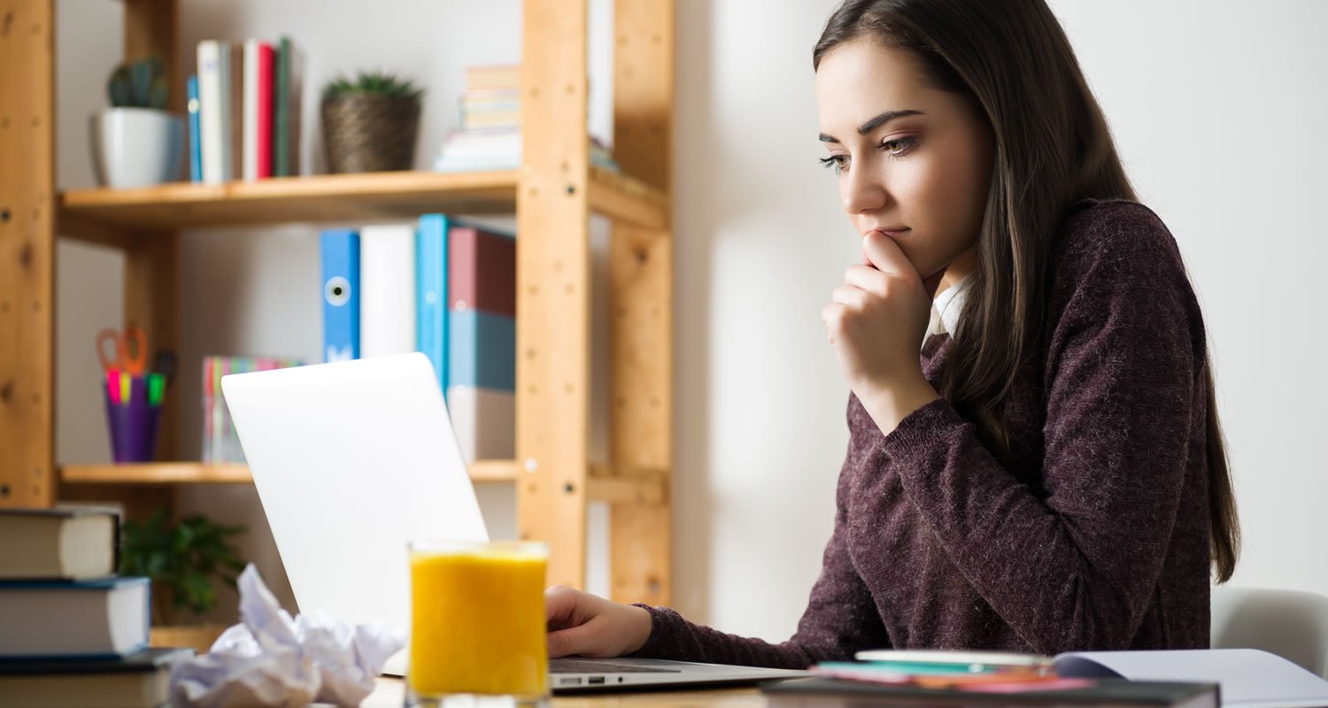 Worried looking girl sat at desk looking at laptop