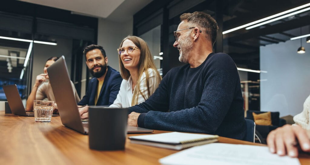 Professionals sat at table in a meeting with laptops
