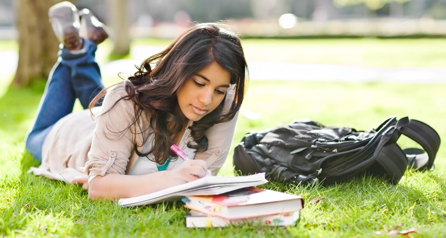 Student laying on grass writing in notebook